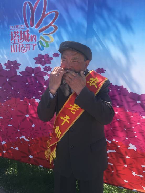 卡弯　·　沙德克老支书参加“塔城的山花开了　丰蕴塔城”活动时，从口袋掏出一把口琴，吹奏一曲《歌唱祖国》。